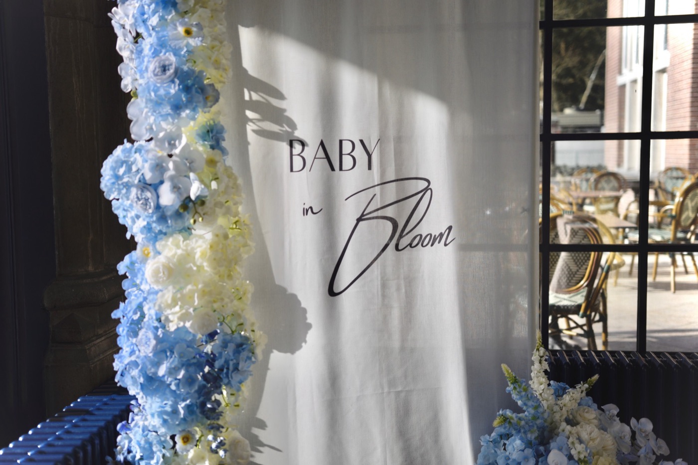 Witte doek met de tekst Baby in Bloom naast een zuil van blauwe en witte bloemen