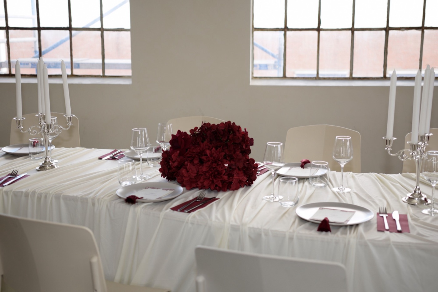 Gedekte tafel met bordeauxrode bloemen, servetten en zilveren kandelaars voor grote ramen