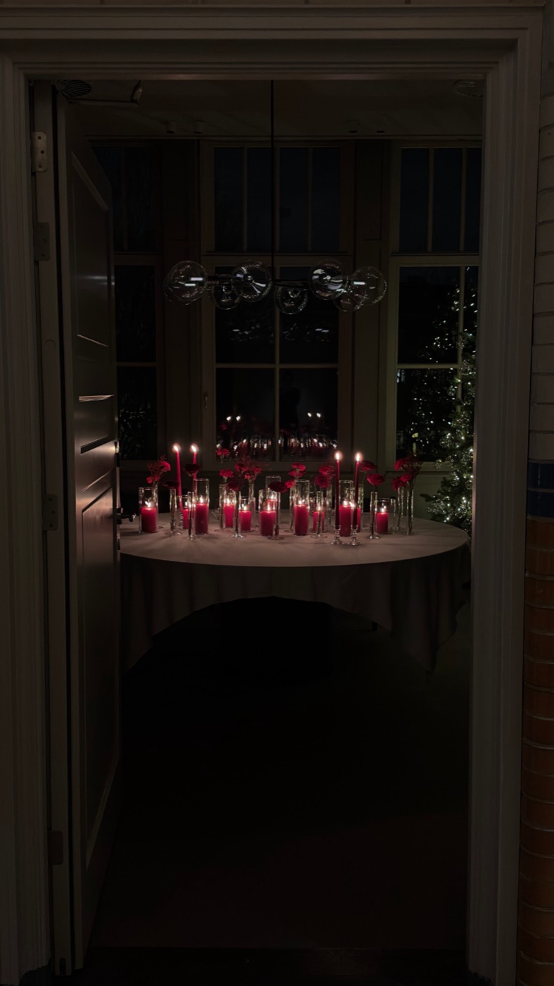 Doorkijk door een deuropening naar een ronde tafel vol rode kaarsen bij een kerstboom