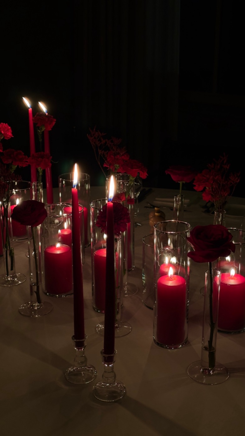 Rode kaarsen in glazen cilinders, taperkaarsen en losse rode bloemen op een tafel