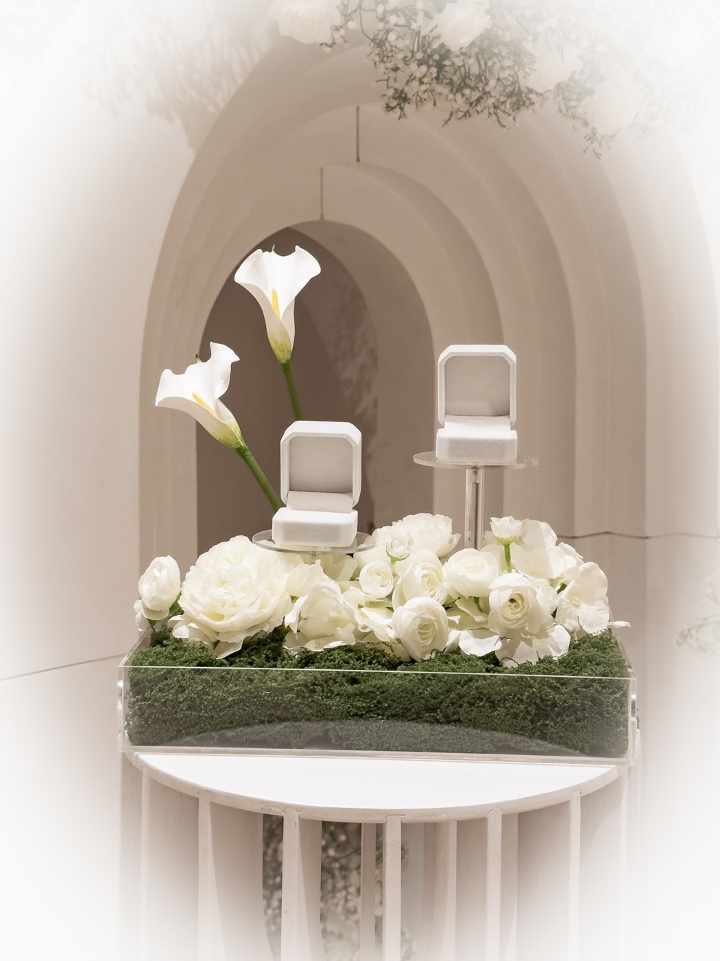 Twee ringdoosjes op een bed van witte bloemen en mos, voor een witte boog