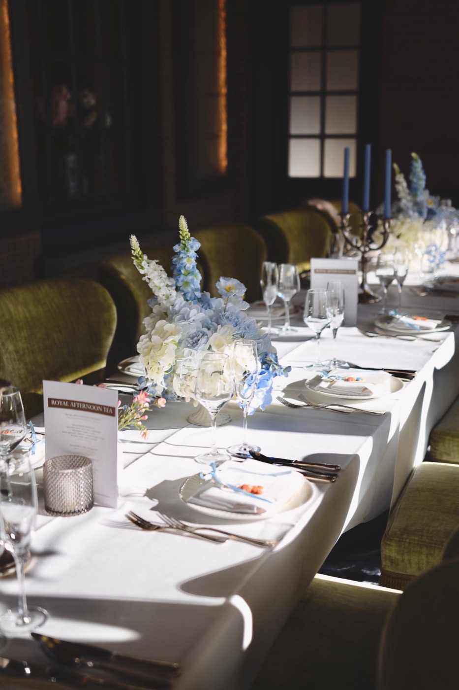 Lange gedekte tafel met blauw-witte bloemstukken, menukaarten en blauwe kaarsen