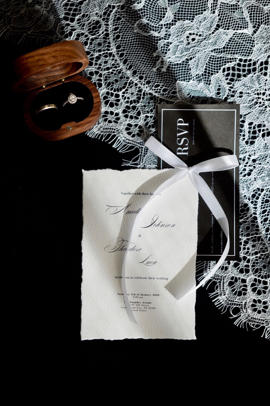 Trouwuitnodiging met wit lint, RSVP-kaart en ringendoosje op zwart kant